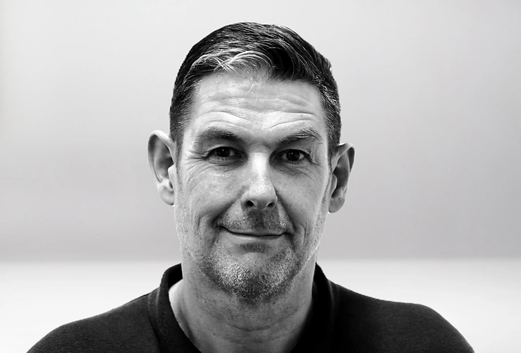 Black and white portrait of Silent Warrior founder Darren Diprose smiling, wearing a dark shirt.